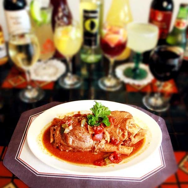 Cuban Ropa Vieja, shredded beef in tomato sauce, garnished with parsley, with drinks in the background.